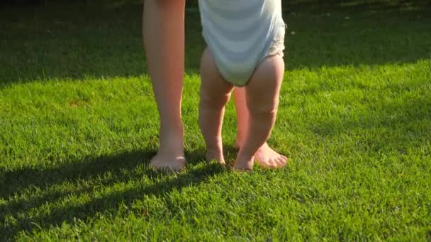Close-up van blote voeten baby jongen en moeder staan op vers groen gras in het park. Begrip gezonde levensstijl, ontwikkeling van kinderen en ouderschap. — Stockvideo