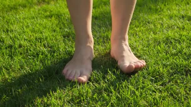 Sıcak yaz gününde çıplak ayaklı bir kadının taze yeşil çimlerin tadını çıkarması. Sağlıklı yaşam tarzı, özgürlük ve doğada rahatlama kavramı. — Stok video