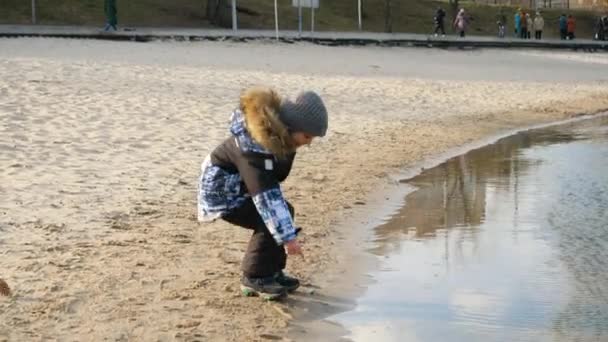 Joyeux garçon souriant touchant l'eau froide dans l'étang au parc le jour venteux d'hiver — Video