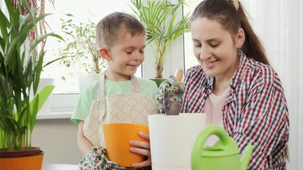 Mladá matka učí svého syna přesazovat květiny do květináčů doma. Koncept zahradničení, hobby, domácí výsadba. — Stock video