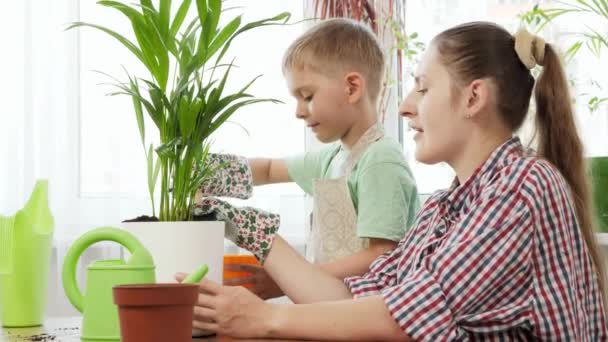 Kisfiú kertész anyával, aki virágcserépbe önti a földet. A kertészkedés, a hobbi, az otthoni ültetés fogalma. — Stock videók