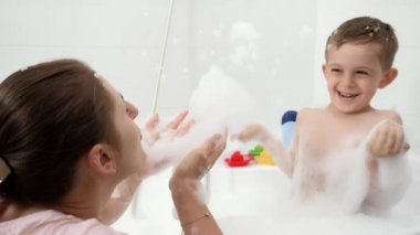 Annesiyle banyo köpüğüyle kavga eden neşeli bir çocuk. Hijyen kavramı, çocuk gelişimi ve evde eğlence