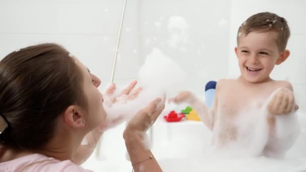 Veselý chlapec s matkou se hádají s mýdlovou pěnou ve vaně. Koncept hyginu, vývoje dětí a zábavy doma — Stock video