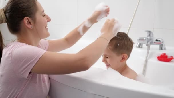Glücklich lächelnde Mutter, die ihrem Sohn beim Waschen im Badezimmer stylische Frisuren schneidet. Konzept aus Hygiene, kindlicher Entwicklung und Spaß zu Hause — Stockvideo