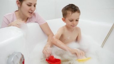 Küçük çocuk banyoda yıkanırken annesiyle ve oyuncaklarıyla oynuyor. Aile zamanı kavramı, çocuk gelişimi ve evde eğlence