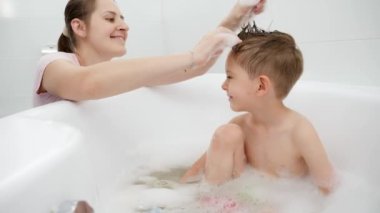Mutlu gülümseyen anne oğluyla oynayıp sabun köpüğüyle banyo yapıyor. Aile zamanı kavramı, çocuk gelişimi ve evde eğlence