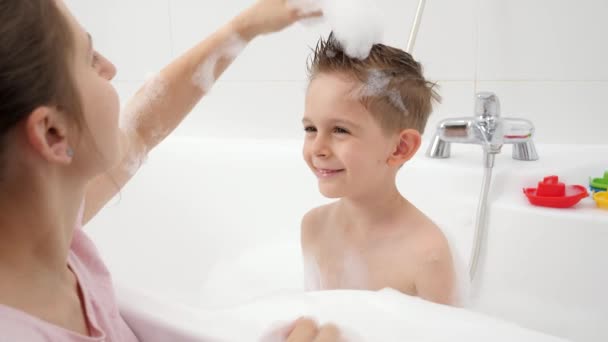 Felice madre sorridente con figlio che gioca in bagno e fare tagli di capelli alla moda con schiuma di sapone. Concetto di hygine, sviluppo bambini e divertimento a casa — Video Stock