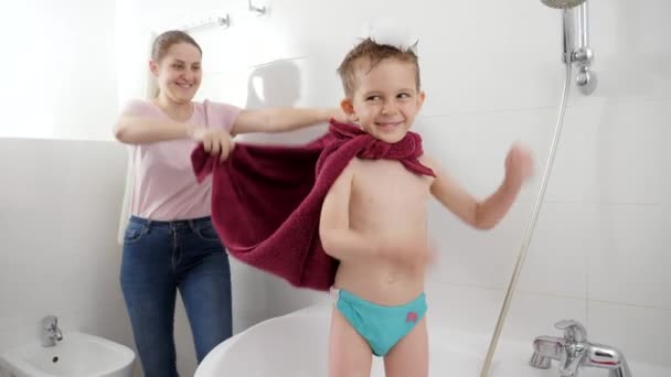 Vtipný chlapeček předstírající, že je superhrdina s matkou v koupelně. Koncept rodinného času, vývoje dětí a zábavy doma — Stock video