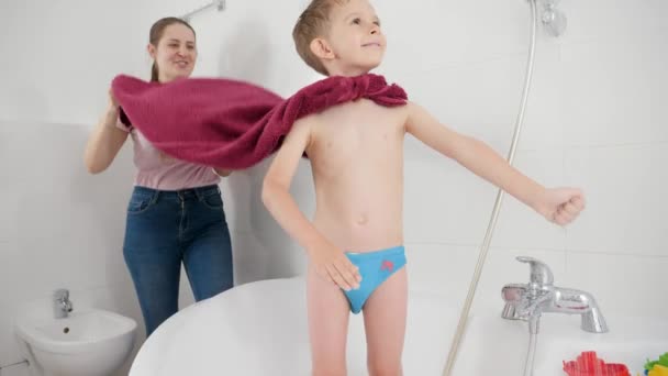 Lustiger lächelnder Junge mit Mutter, die im Superhelden spielt, während sie sich im Badezimmer unter der Dusche wäscht. Konzept Familienzeit, Entwicklung der Kinder und Spaß zu Hause — Stockvideo