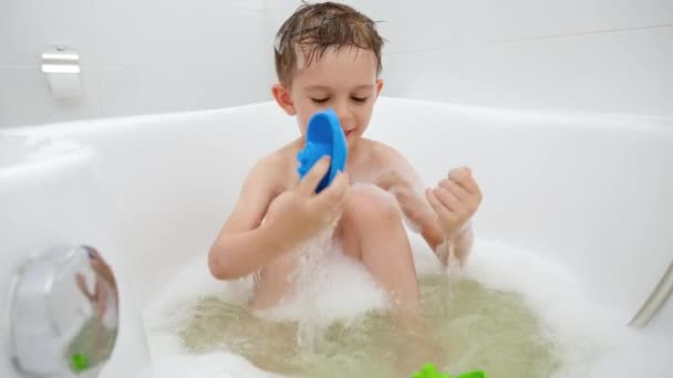 Ragazzo carino godersi il bagno con schiuma di sapone e giocattoli. Concetto di tempo in famiglia, sviluppo dei bambini e divertimento a casa — Video Stock