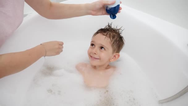 Matka nakłada szampon i myje głowę syna w wannie. Pojęcie hygine, rozwoju dzieci i zabawy w domu — Wideo stockowe