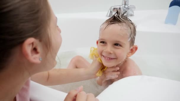 Šťastný usmívající se chlapec dívá na matku, zatímco ona ho myje mýdlem a houbou v koupelně. Koncept hyginu, vývoje dětí a zábavy doma — Stock video