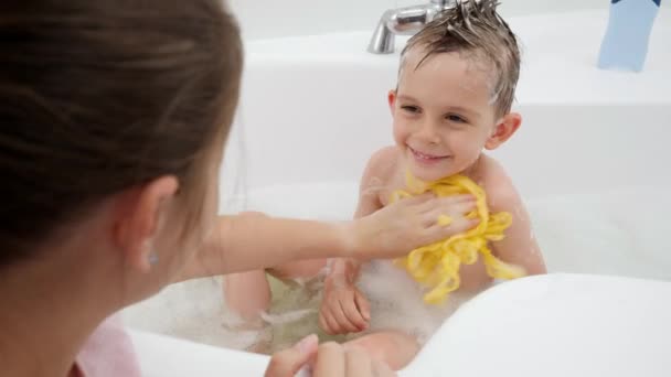 Junge Mutter wäscht ihren kleinen Sohn mit Seife und gelbem Schwamm im Bad. Konzept aus Hygiene, kindlicher Entwicklung und Spaß zu Hause — Stockvideo