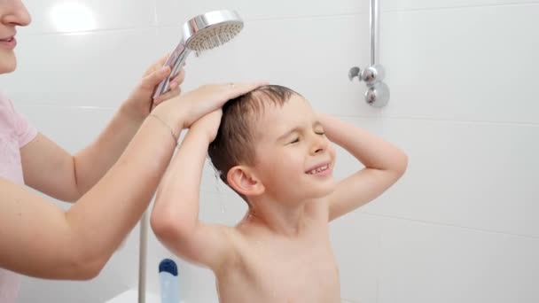Ragazzino con madre che si strofina la testa e lava i capelli con lo shampoo sotto la doccia. Concetto di hygine, sviluppo bambini e divertimento a casa — Video Stock