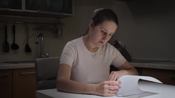 Mulher confusa examina documentos financeiros na cozinha à noite. Conceito de dificuldades financeiras, falência, impostos e rendas. — Vídeo de Stock