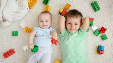 Bebek ve büyük çocuğun portresi halıda renkli oyuncakların ve tuğlaların yanında uzanmış kameraya bakıyordu. Çocuk gelişimi, eğitim ve yaratıcılık kavramı