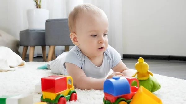 Маленький хлопчик грає з різнокольоровими іграшковими машинами на килимі у вітальні. Концепція розвитку дітей, виховання та творчість вдома — стокове фото