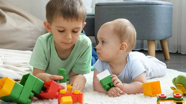 Little boy with baby brother building tower from toy blocks and bricks on floor in living room. Concept of children development, education and creativity at home — Stock Photo, Image