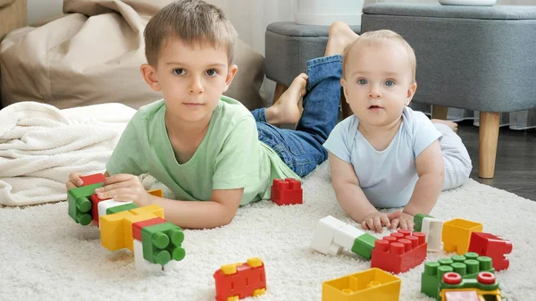 Šťastný chlapec s bratříčkem stavět dům z barevných hraček cihly a bloky. Koncepce vývoje, vzdělávání a tvořivosti dětí doma — Stock fotografie