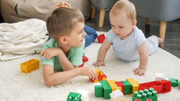 Šťastný usměvavý chlapeček se starším bratrem hrající hračky na koberci v obýváku. Koncepce vývoje, vzdělávání a tvořivosti dětí doma — Stock fotografie