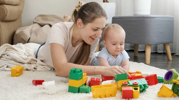 Szczęśliwa uśmiechnięta matka z synkiem budującym zabawkową wieżę z kolorowych cegieł i klocków. Koncepcja rozwoju, edukacji i kreatywności dzieci w domu — Zdjęcie stockowe