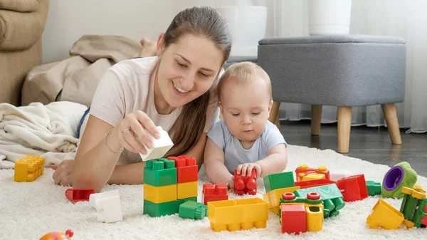 Feliz sorrindo mulher brincando com seu menino no tapete e construindo torre de brinquedo com blocos e tijolos. Conceito de desenvolvimento infantil, educação e criatividade em casa — Fotografia de Stock