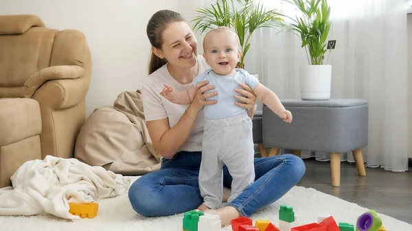 Bonito menino sorridente em pé na sala de estar e olhando para brinquedos coloridos. Conceito de desenvolvimento infantil, educação e criatividade em casa — Fotografia de Stock