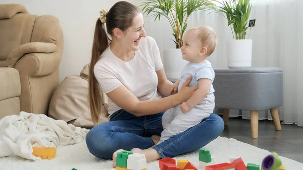 Bébé garçon souriant mignon assis sur les genoux des mères et regardant des jouets colorés. Concept de développement, d'éducation et de créativité des enfants à la maison — Photo