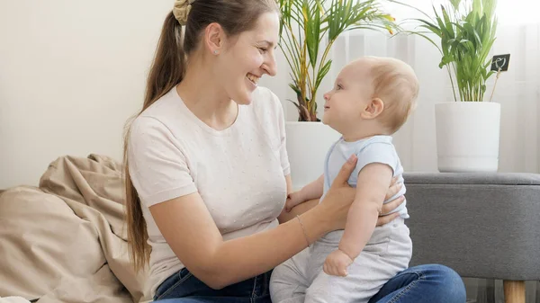 Feliz madre sonriente sosteniendo y meciendo a su pequeño hijo en el regazo en la sala de estar. Concepto de desarrollo infantil, educación y creatividad en el hogar — Foto de Stock