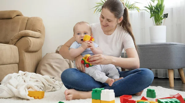 Jonge lachende moeder die thuis met haar zoontje speelt in speelgoedauto 's. Het begrip gezin dat tijd samen heeft en de ontwikkeling van kinderen — Stockfoto