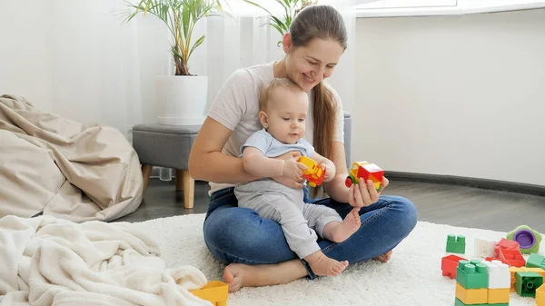 Madre sonriente sentada en la alfombra y jugando con su pequeño hijo en coches de juguete. Concepto de familia teniendo tiempo juntos y desarrollo de los niños — Foto de Stock