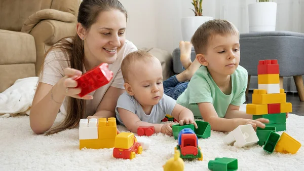 Счастливая улыбающаяся семья с ребенком, играющим на ковре с игрушечными блоками, бричками и машинами. Концепция семейного времяпровождения и развития детей — стоковое фото