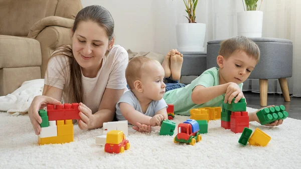 Uśmiechnięte wesołe dziecko, chłopiec i matka palą zabawki na dywanie w domu. Pojęcie rodziny spędzającej razem czas i rozwoju dzieci — Zdjęcie stockowe