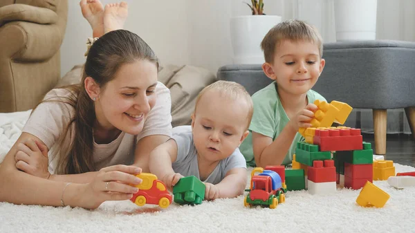 Wesoła uśmiechnięta rodzina bawiąca się zabawkami i zabawą na dywanie razem w domu. Pojęcie rodziny spędzającej razem czas i rozwoju dzieci — Zdjęcie stockowe