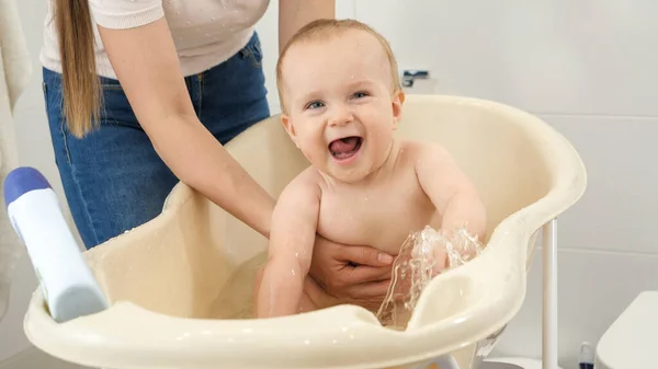 Feliz niño riéndose sentado en un baño de plástico y salpicando agua. Concepto de higiene infantil, atención sanitaria y crianza de los hijos. — Foto de Stock