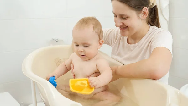 Feliz madre sonriente mirando a su hijo jugando con juguetes en el baño — Foto de Stock