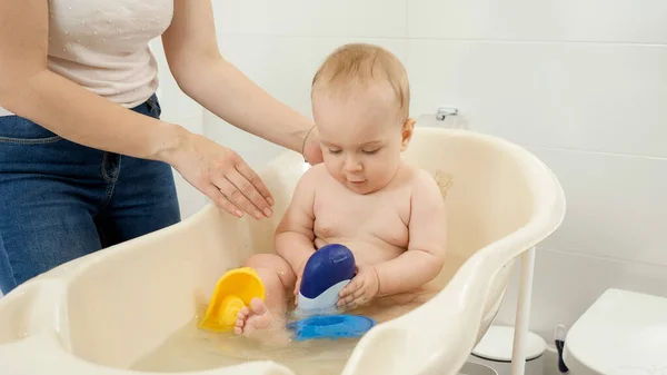 Lindo bebé niño sentado en el baño y jugando con champú y botellas de gel de ducha — Foto de Stock