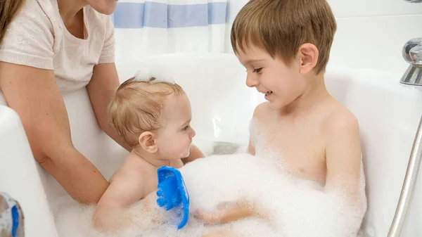 Lindo bebé y hermano mayor lavando y jugando en baño con espuma. Concepto de higiene infantil, atención sanitaria y atención familiar en el hogar — Foto de Stock