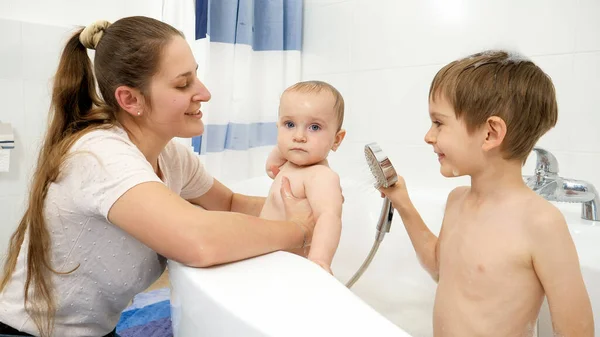 Starszy chłopiec pomaga matce myć młodszego brata w wannie z prysznicem. Pojęcie higieny dzieci, opieki zdrowotnej i opieki rodzinnej w domu — Zdjęcie stockowe