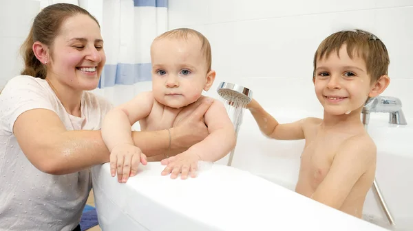 Glücklich lächelnde Mutter und älterer Sohn beim Waschen des kleinen Bruders in der Badewanne. Konzept der Kinderhygiene, Gesundheitsfürsorge und häuslichen Pflege — Stockfoto