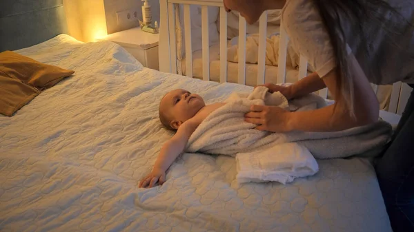 Az anya az ágyon fekszik a kisfiát törölközővel beborítva, miután fürdött. A gyermekhigiénia, az egészségügyi ellátás és a családi gondozás fogalma otthon — Stock Fotó