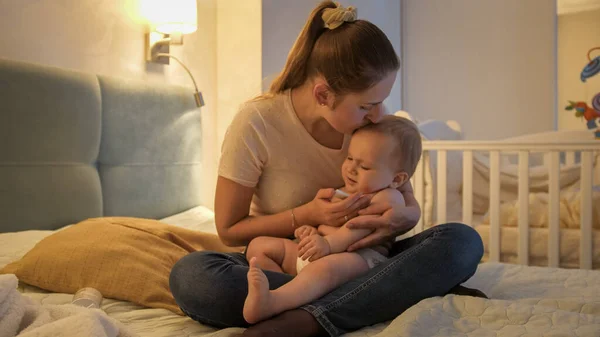 Молодая любящая мать целует своего сына, измеряя его температуру термометром — стоковое фото