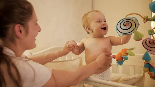 Słodki chłopiec i matka bawią się kolorowymi zabawkami w łóżeczku niemowlęcym. Koncepcja rodzicielstwa, rozwój dzieci. — Zdjęcie stockowe