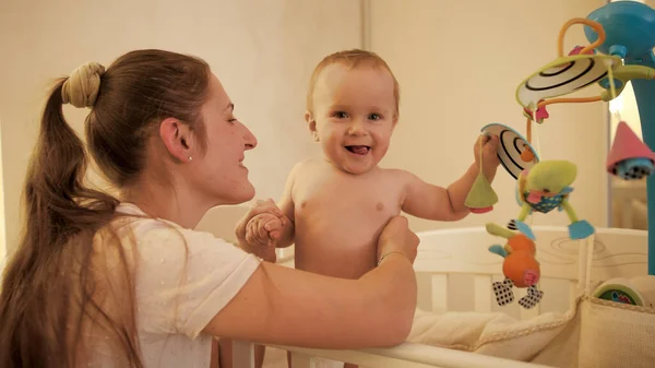 Glücklich lächelnder kleiner Junge in Windeln, der in der Krippe steht und mit sich drehenden Spielzeugen spielt — Stockfoto