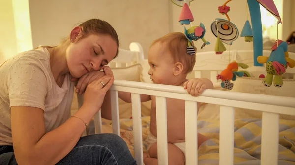 Little baby boy looking at his mother sleeping on the bed side at night — Stock Photo, Image