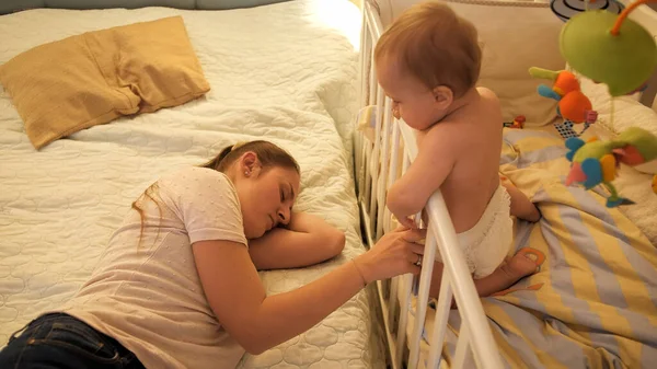 Бессонный мальчик, глядя на мать, уснул, качая его в кроватке. — стоковое фото