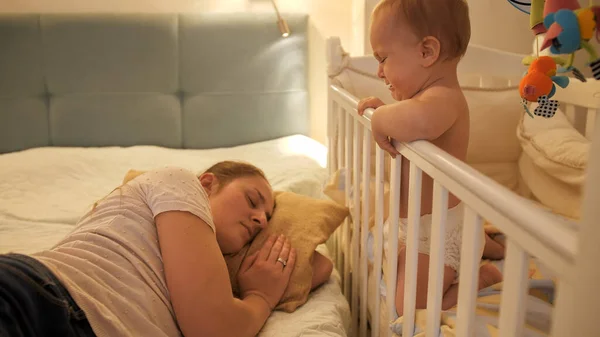 울고 있는 어린 소년 이 엄마가 밤에 침대에서 자고 있는 것을 깨운다. 육아에 대한 개념, 부모 의피로 및 자녀 발육. — 스톡 사진