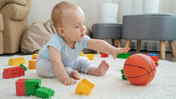 Szczęśliwy uśmiechnięty chłopiec bawiący się zabawkami i koszykówką na dywanie w domu. Koncepcja rozwoju dzieci, sportu, edukacji i kreatywności w domu — Zdjęcie stockowe