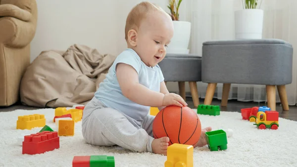 Cheerful baby boy playing and having fun with basketball on floor at living room. Concept of children development, sports, education and creativity at home — Stock Photo, Image