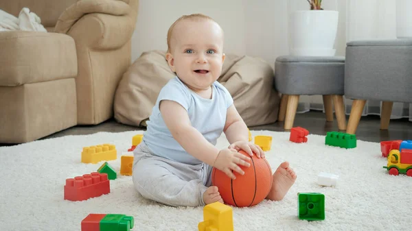 Улыбающийся веселый мальчик веселится на ковре и играет с мячом. Концепция развития детей, спорта, образования и творчества на дому — стоковое фото